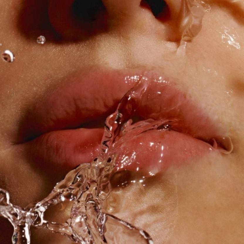 Close-up of a person's mouth with water splashing into it